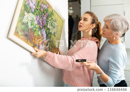Mother and daughter putting picture on wall Mother and daughter putting picture on wall 138698486