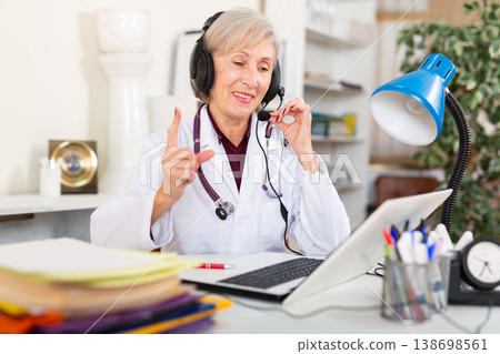 Smiling aged female doctor in headset conducting online consultation 138698561