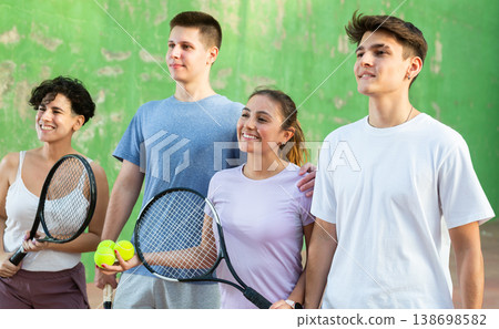 Happy frontenis players with rackets and balls standing in open court 138698582