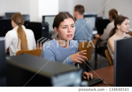 Young woman student of computer courses looks at monitor screen, types on keyboard and does work Young woman student of computer courses looks at monitor screen, types on keyboard and does work 138698583
