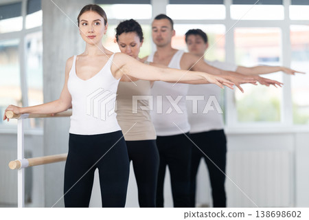 Pretty young girl in black and white sportswear, participating 2nd position of ballet stance at barre with group in choreography studio Pretty young girl in black and white sportswear, participating 2nd position of ballet stance at barre with group in choreography studio 138698602