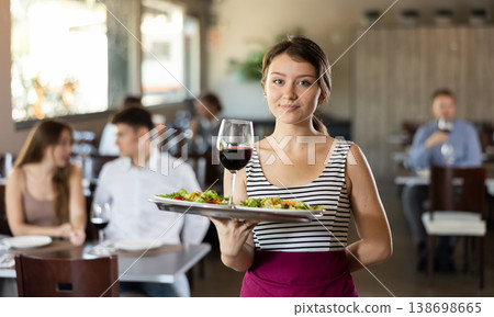 Waitress standing with salad and glass of wine on serving tray in restaurant 138698665