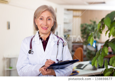 Woman doctor standing in medical office making notes on clipboard closeup Woman doctor standing in medical office making notes on clipboard closeup 138698677