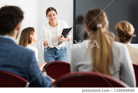 Positive skilled female coach explaining topic to group of people during foreign language class in auditory Positive skilled female coach explaining topic to group of people during foreign language class in auditory 138698686