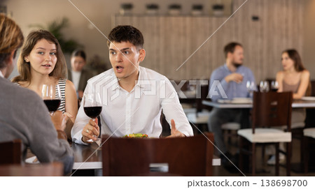 Three friends meeting in modern restaurant - men and woman drinking wine, talking, discussing problems 138698700