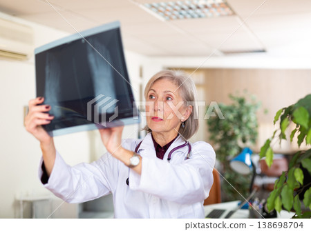 Aged female traumatologist looking at x-ray of foot in clinic office Aged female traumatologist looking at x-ray of foot in clinic office 138698704