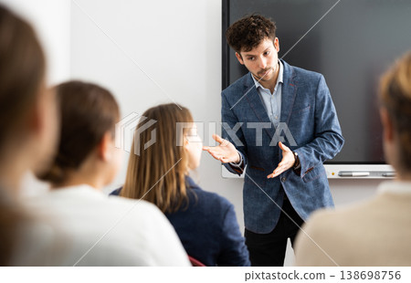 Young male tutor teaching students in college classroom Young male tutor teaching students in college classroom 138698756