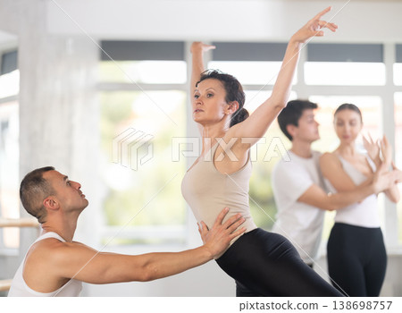 Portrait of young man practicing in classical ballet pose with support with young beautiful woman in black and white clothing in ballet hall 138698757