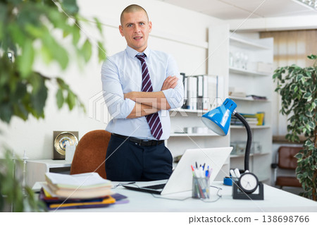 Portrait of male businessman who is standing near his workplace in office 138698766
