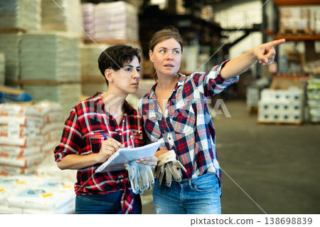 Woman manager discussing order list with female worker at warehouse of building materials Woman manager discussing order list with female worker at warehouse of building materials 138698839