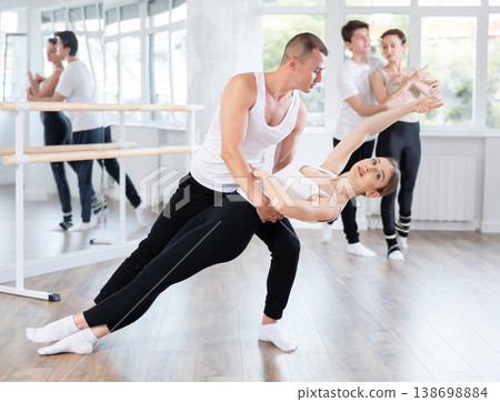 Happy ballet dancers couple performing choreography with support during group training classes in dance studio Happy ballet dancers couple performing choreography with support during group training classes in dance studio 138698884
