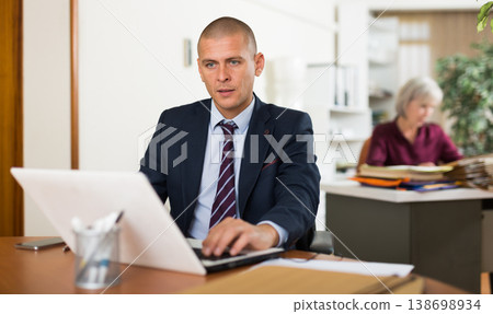 Male clerical worker sitting and using laptop Male clerical worker sitting and using laptop 138698934