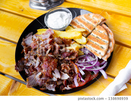 Meat souvlaki served with French fries, onions and pita bread Meat souvlaki served with French fries, onions and pita bread 138698939