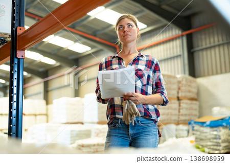 Woman standing in warehouse and holding documents in hands Woman standing in warehouse and holding documents in hands 138698959