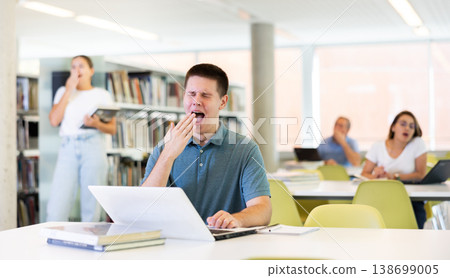 Young male student yawns out of boredom in public library Young male student yawns out of boredom in public library 138699005