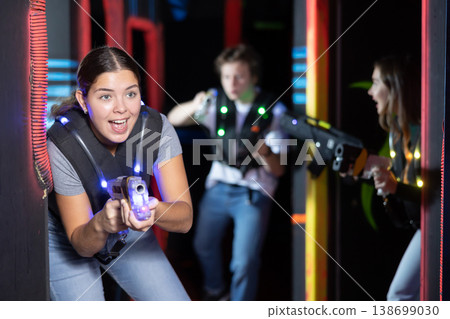Smiling girl with laser pistol during playing laser tag with her friends in room 138699030