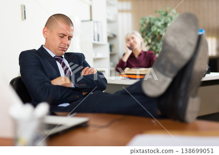 Office employee in formal suit sleeping at workplace with legs on table Office employee in formal suit sleeping at workplace with legs on table 138699051