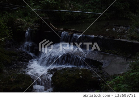 A clear stream flows down from a dam in a dimly lit gorge. A clear stream flows down from a dam in a dimly lit gorge. 138699751
