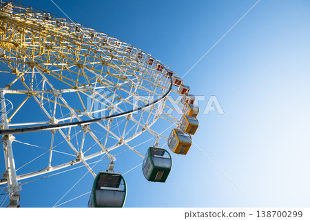 Upward view of green, yellow, and orange cabins on a large observation wheel 138700299