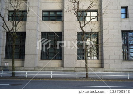 The imposing stone exterior walls of the modern building and the winter street trees lining the sidewalks The imposing stone exterior walls of the modern building and the winter street trees lining the sidewalks 138700548