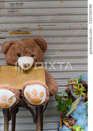 A teddy bear holding a cafe sign placed in front of a shutter. 138700596