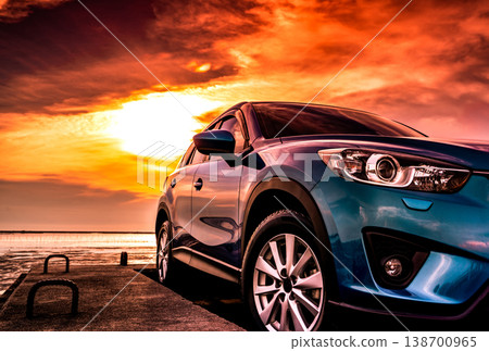 Blue compact SUV car with sport, modern, and luxury design parked on concrete road by the sea at sunset. Front view of beautiful hybrid car. Driving with confidence. Travel on vacation at the beach. 138700965