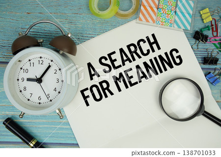 A Search For Meaning text on a paper surrounded by office supplies, a magnifying glass, and a clock on a blue wooden surface A Search For Meaning text on a paper surrounded by office supplies, a magnifying glass, and a clock on a blue wooden surface 138701033