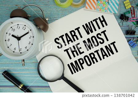 Start With The Most Important text on a paper surrounded by office supplies, a magnifying glass, and a clock on a blue wooden surface Start With The Most Important text on a paper surrounded by office supplies, a magnifying glass, and a clock on a blue wooden surface 138701042