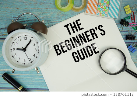 The Beginners Guide text on a paper surrounded by office supplies, a magnifying glass, and a clock on a blue wooden surface' The Beginners Guide text on a paper surrounded by office supplies, a magnifying glass, and a clock on a blue wooden surface' 138701112