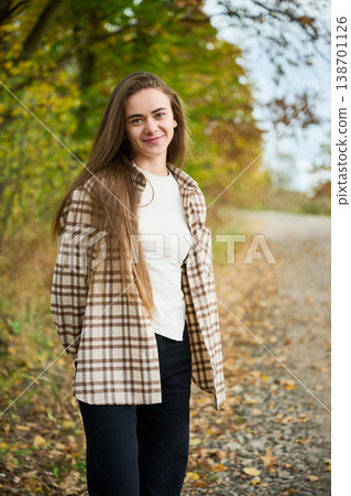 Portrait of young woman standing on rural path with autumn foliage, soft natural light and warm colors, casual lifestyle scene, concept of calmness and freedom Portrait of young woman standing on rural path with autumn foliage, soft natural light and warm colors, casual lifestyle scene, concept of calmness and freedom 138701126