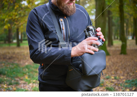 Man placing drone into shoulder bag in park, packing quadcopter after use, preparing equipment for transport, technology and hobby concept 138701127