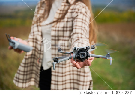 Close up of woman holding flying drone toward camera with spinning propellers and controller in hand, shallow depth of field, concept of modern technology and hobby Close up of woman holding flying drone toward camera with spinning propellers and controller in hand, shallow depth of field, concept of modern technology and hobby 138701227