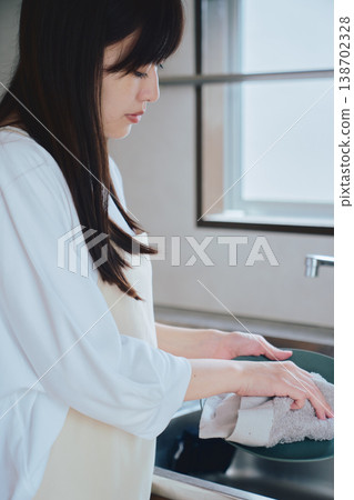 A woman washing dishes in the kitchen: A scene depicting everyday household chores and a mindful lifestyle. 138702328