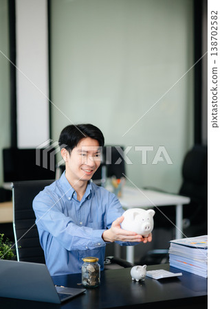 Smiling businessman saves money with piggy bank and coins; ideal for themes of finance, savings, budgeting, Smiling businessman saves money with piggy bank and coins; ideal for themes of finance, savings, budgeting, 138702582