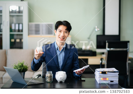 Smiling businessman saves money with piggy bank and coins; ideal for themes of finance, savings, budgeting, Smiling businessman saves money with piggy bank and coins; ideal for themes of finance, savings, budgeting, 138702583