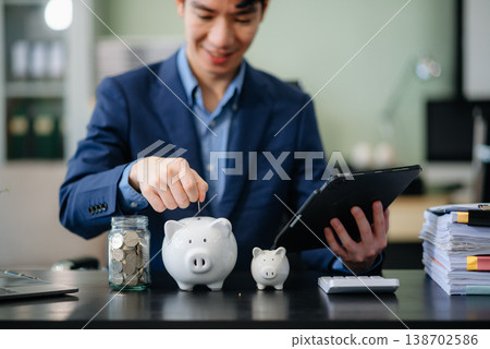 Smiling businessman saves money with piggy bank and coins; ideal for themes of finance, savings, budgeting, 138702586