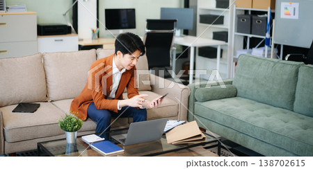 Confident young businessman working on a laptop, analyzing documents in a stylish modern office. Confident young businessman working on a laptop, analyzing documents in a stylish modern office. 138702615