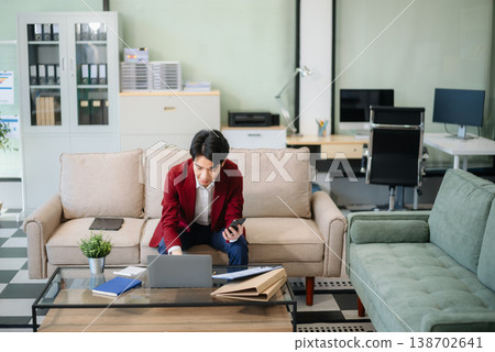 Confident young businessman working on a laptop, analyzing documents in a stylish modern office. Confident young businessman working on a laptop, analyzing documents in a stylish modern office. 138702641