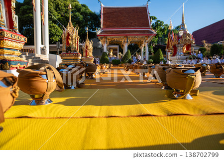 Dozens of covered alms bowls sit spaced across a yellow mat. Silver bases and fabric straps show an organized setup. 138702799