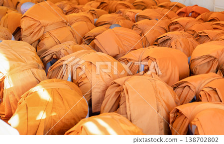 Monks bow forward together in a packed indoor ritual. Orange robes cover the scene in ordered rows. Monks bow forward together in a packed indoor ritual. Orange robes cover the scene in ordered rows. 138702802