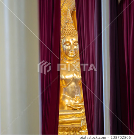 A golden Buddha statue appears between deep red curtains inside the temple. Draped fabric frames the shrine view. A golden Buddha statue appears between deep red curtains inside the temple. Draped fabric frames the shrine view. 138702806