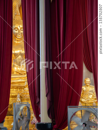 A golden Buddha statue appears between deep red curtains inside the temple. Draped fabric frames the shrine view. A golden Buddha statue appears between deep red curtains inside the temple. Draped fabric frames the shrine view. 138702807
