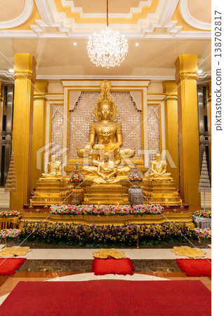A golden Buddha shrine fills the hall with seated statues and flower rows. Chandeliers and columns frame the symmetrical altar. 138702817
