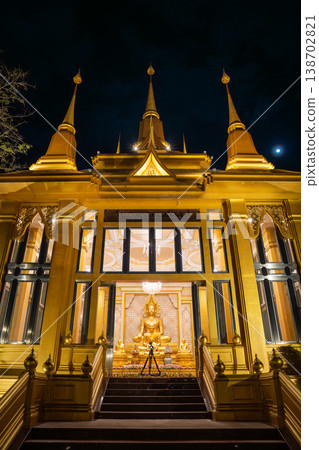 A golden temple entrance rises above dark stairs under the night sky. Lit windows reveal a Buddha shrine inside. 138702821