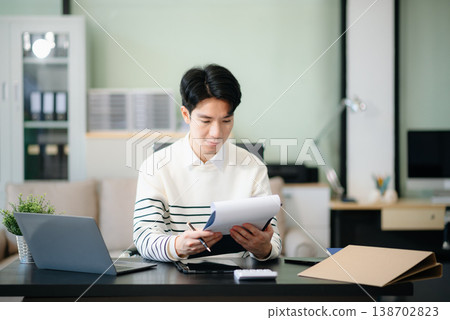 Young handsome man typing on tablet and laptop while sitting at the working table Young handsome man typing on tablet and laptop while sitting at the working table 138702823