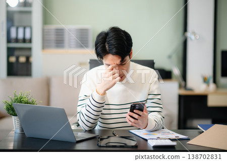 Frustrated young businessman working on a laptop computer sitting at his working place 138702831