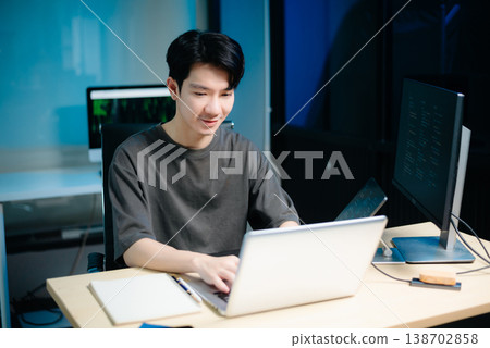 Asian male programmer working with tablet, laptop, and desktop in tech office. Coding, software development 138702858