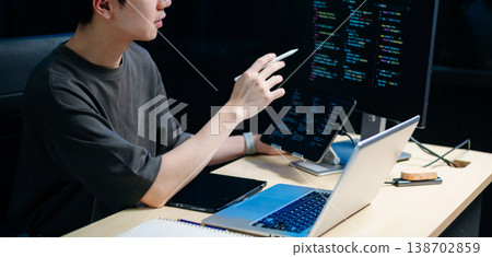 Male programmer using stylus to analyze code on tablet and monitor. Software development, coding, and tech workspace concept 138702859