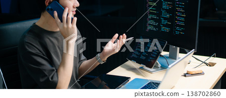 Male programmer using stylus to analyze code on tablet and monitor. Software development, coding, and tech workspace concept 138702860