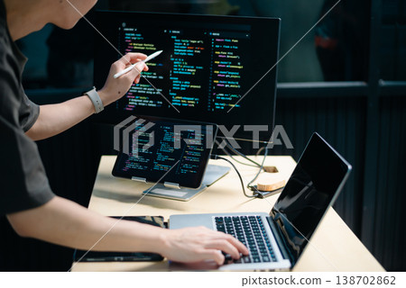 Male programmer using stylus to analyze code on tablet and monitor. Software development, coding, and tech workspace concept 138702862